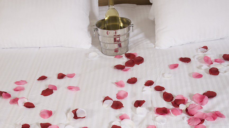 rose petals on bed with bucket of wine